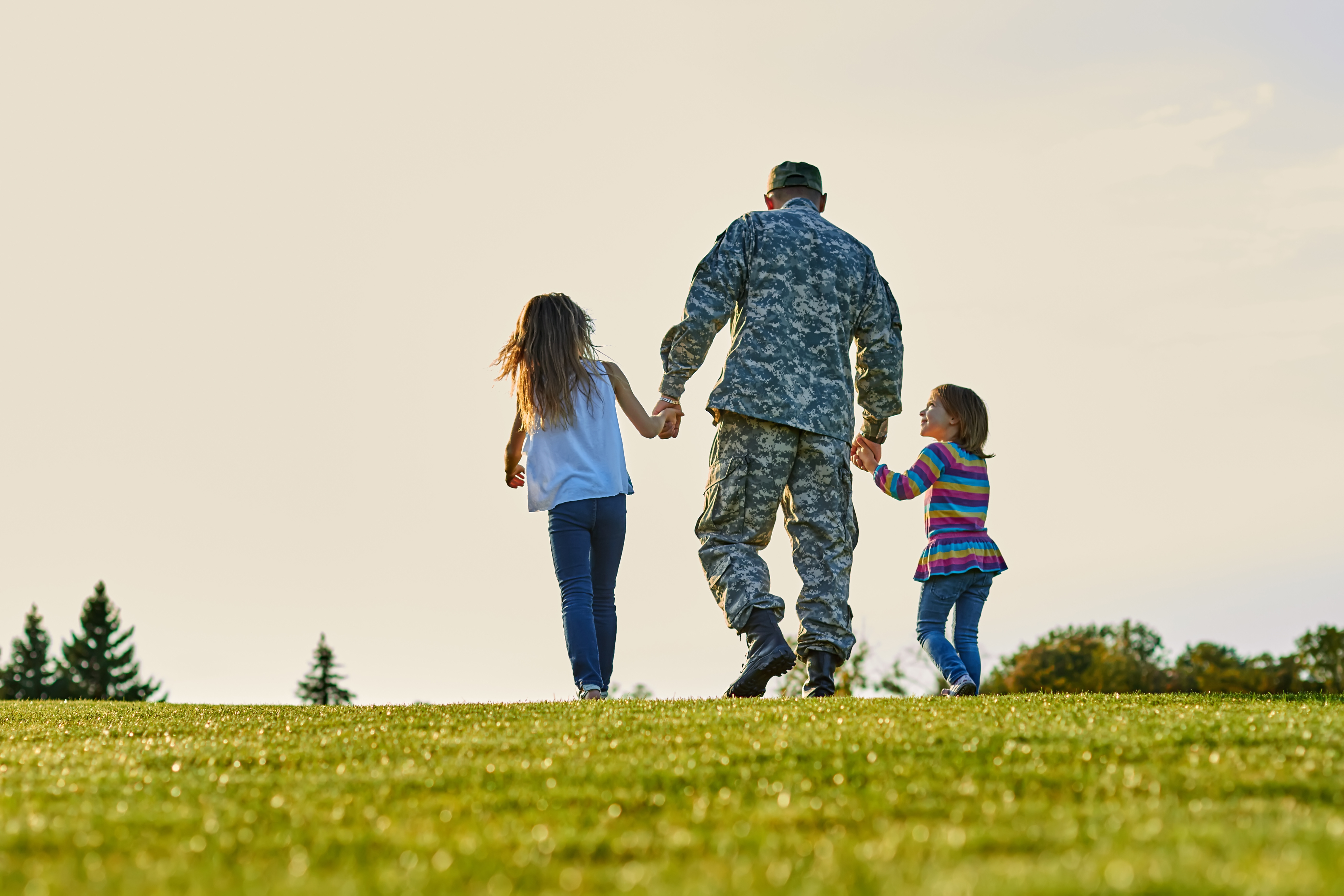 Soldier walking with little girls holding hands.